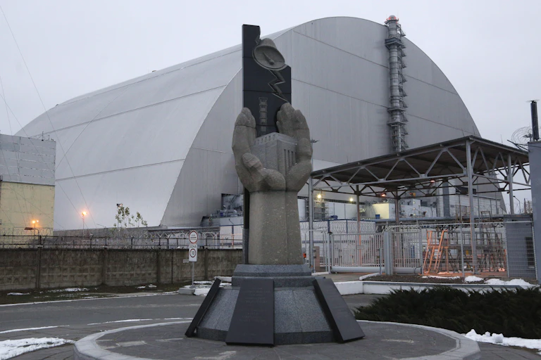 Une statue de mains ouvertes tenant un cube, devant une grande structure en dôme métallique.