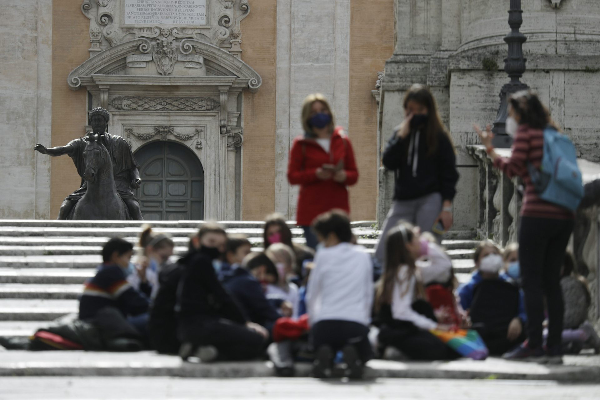 Jóvenes con un adulto visto al aire libre, borrosos sobre una estatua al fondo.