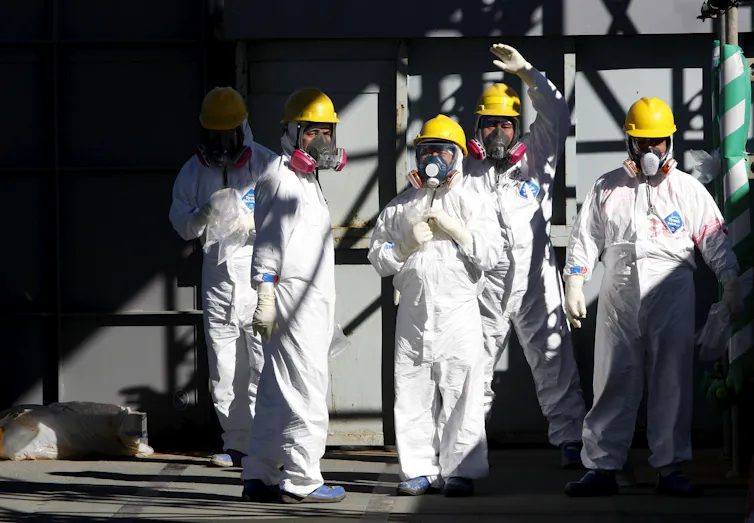 Workers in protective suits and hard hats stand together.