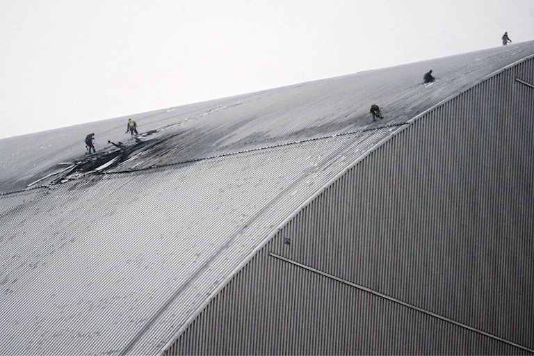 People in protective clothing work on a sloped roof.