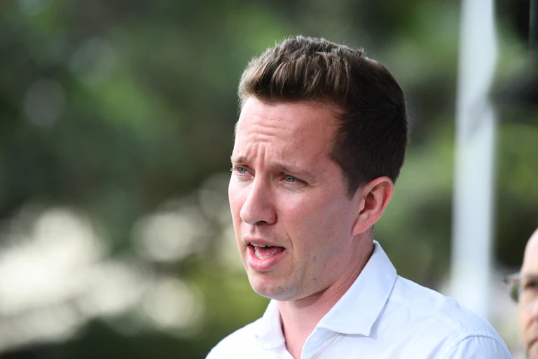 The side-profile of a young man in a white shirt while he addresses media