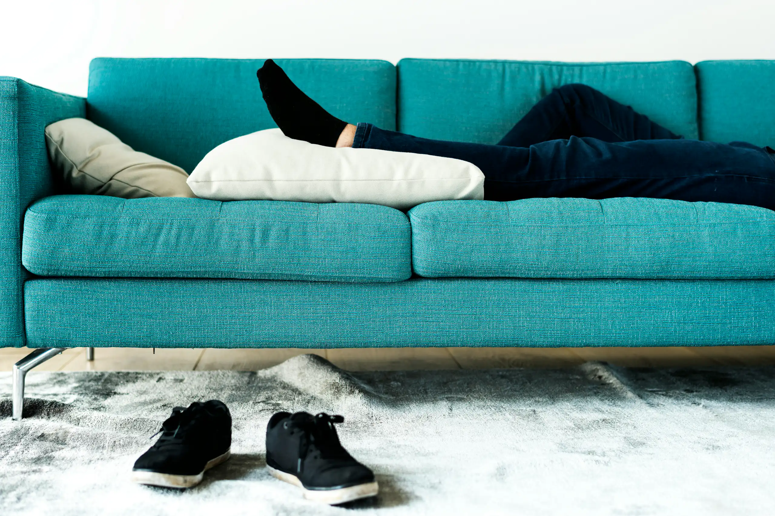A teal sofa showing the legs and feet of a person lying on it