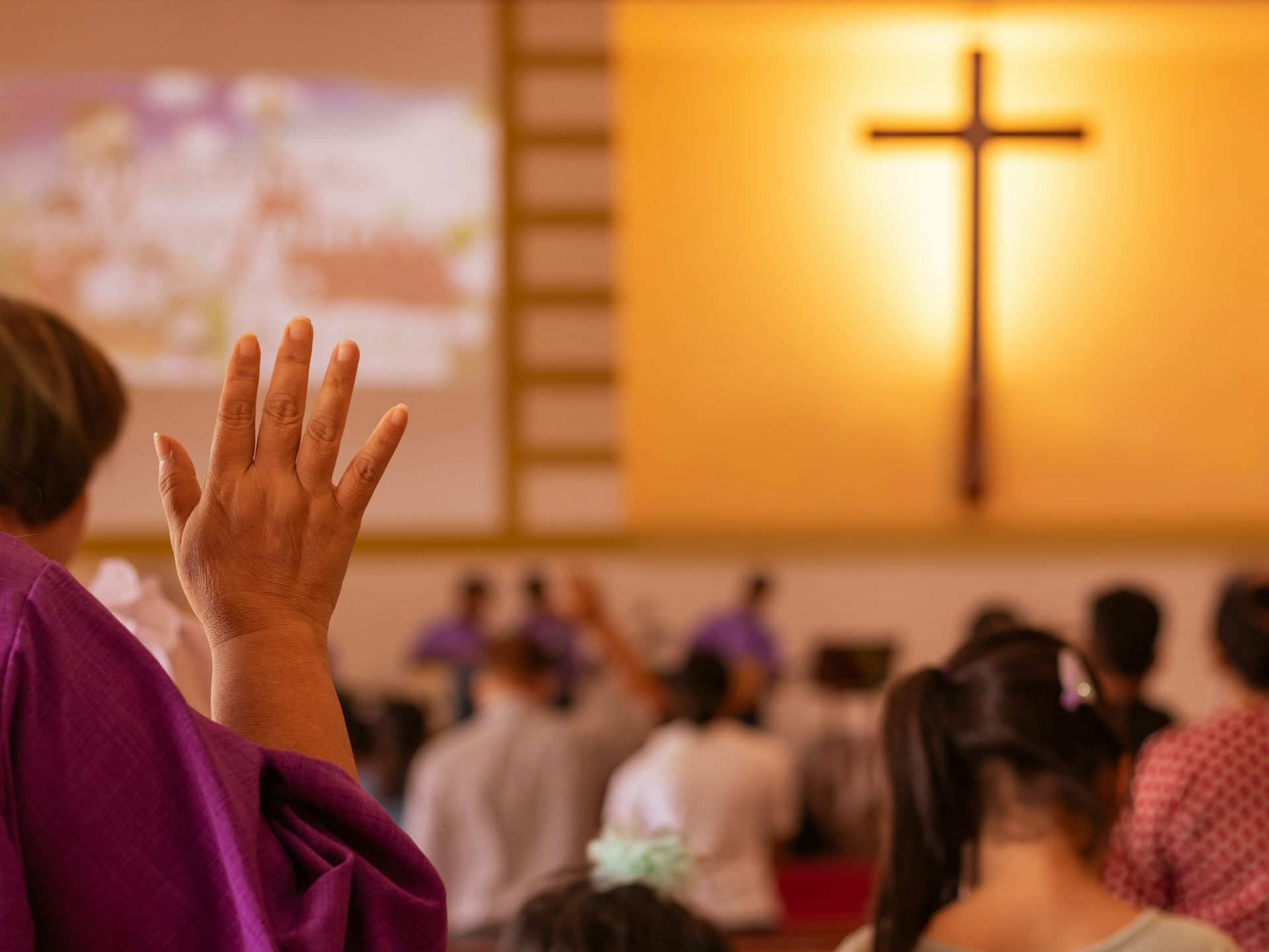 View from behind of diverse group of churchgoers, with a large, illuminated cross on the wall