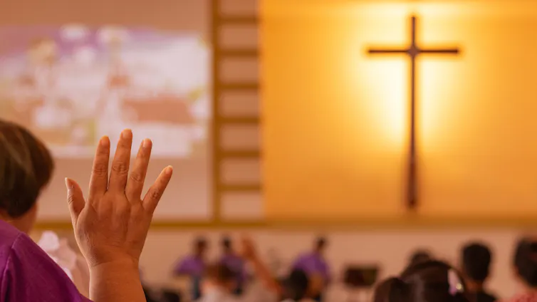 View from behind of diverse group of churchgoers, with a large, illuminated cross on the wall
