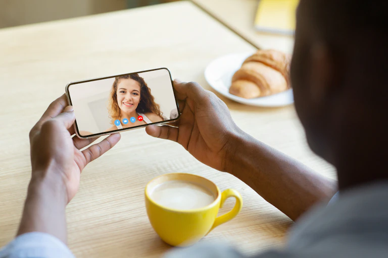 Un homme parlant en visio avec sa petite amie sur son téléphone portable en prenant un café.