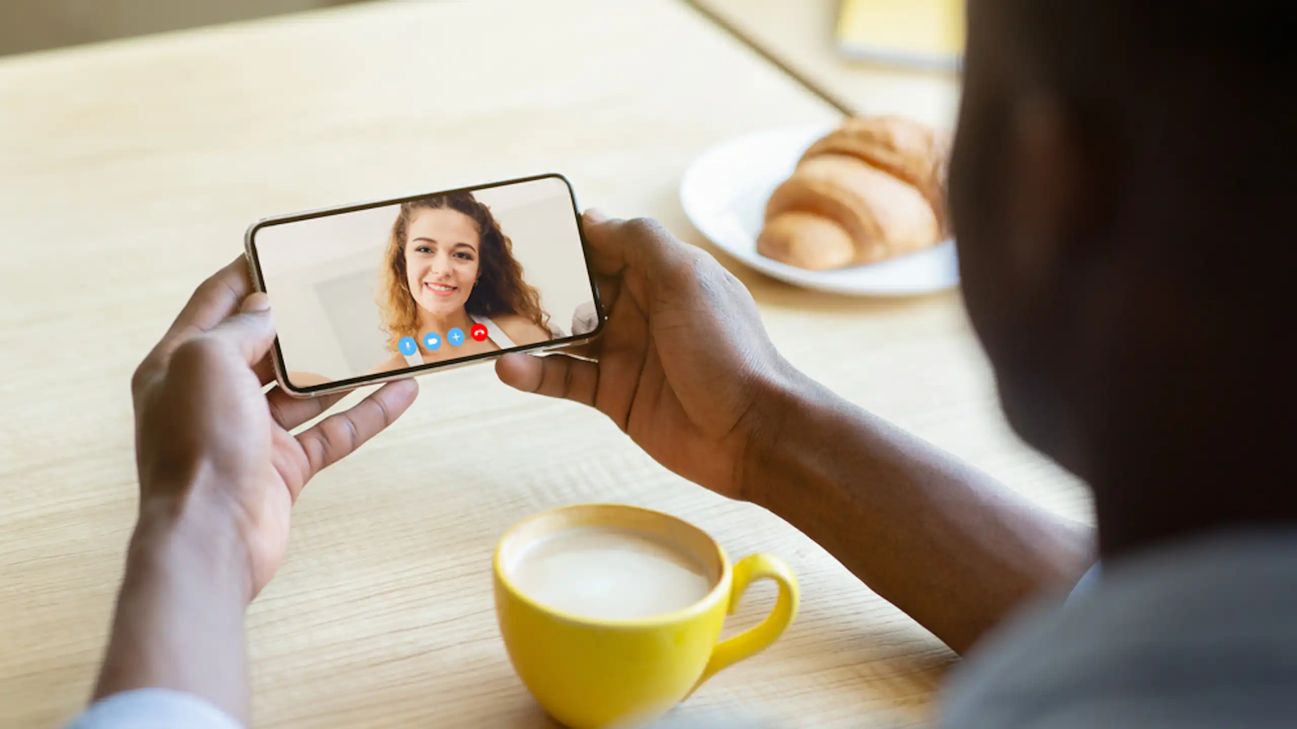 Un homme parlant en visio avec sa petite amie sur son téléphone portable en prenant un café.