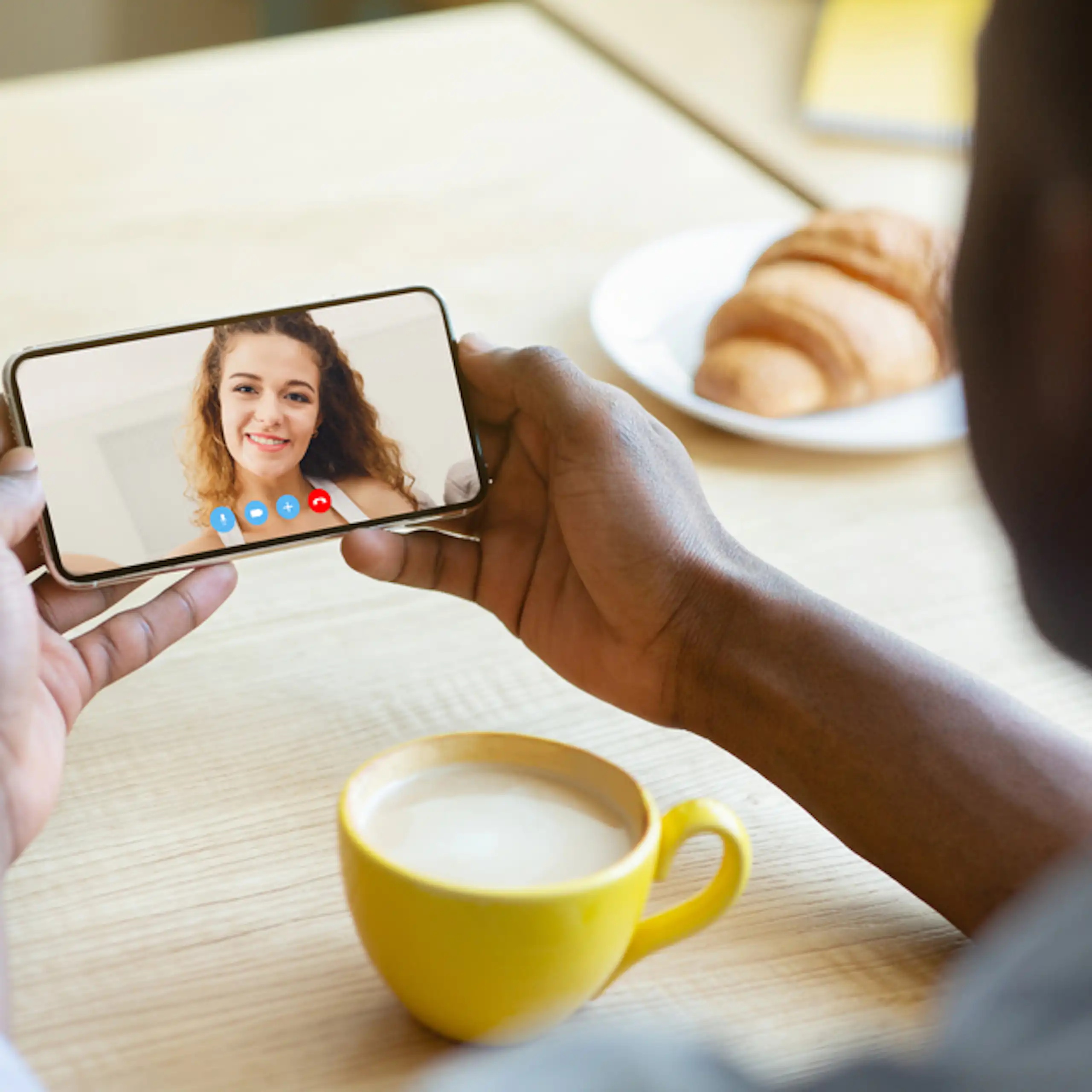 Un homme parlant en visio avec sa petite amie sur son téléphone portable en prenant un café.