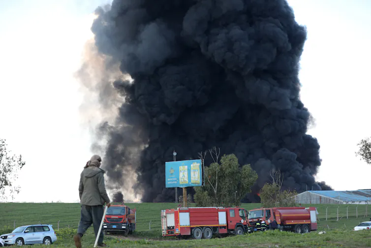 Smoke rises from a warehouse in an open field.