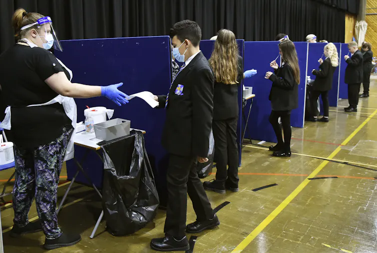 Lo que Canadá, Inglaterra y otros países del G7 han aprendido sobre la construcción de sistemas educativos resilientes durante la pandemia de COVID-19 1 Estudiantes con uniformes escolares vistos en pequeños recintos realizando pruebas de COVID.