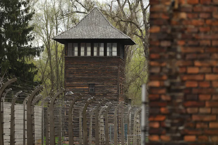 A large brick tower is seen in front of another tower and barbed wire fence.