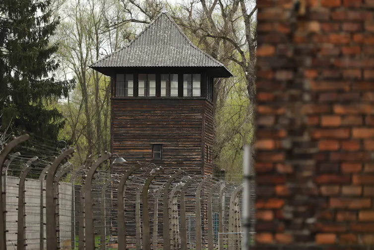 A large brick tower is seen in front of another tower and barbed wire fence.