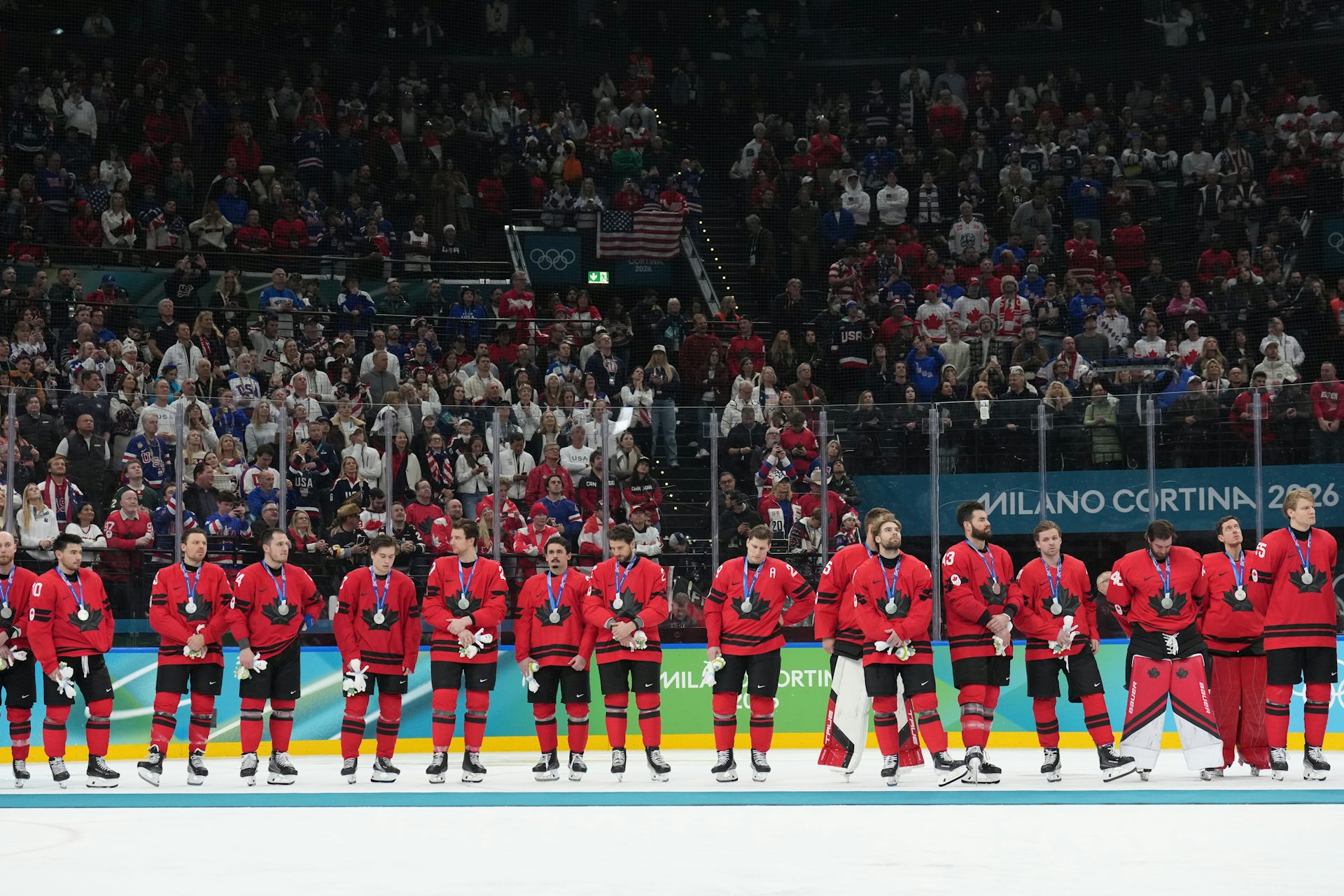 A row of men in red hockey uniforms stand in line on the ice wearing silver medals