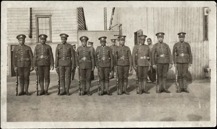 Black and white photo of lines of a posed group of Black soldiers in uniform.