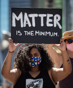 A Black woman at a rally holds a sign that says 'matter is the minimum.'