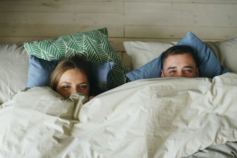 A couple lie in bed covered by a cosy duvet.