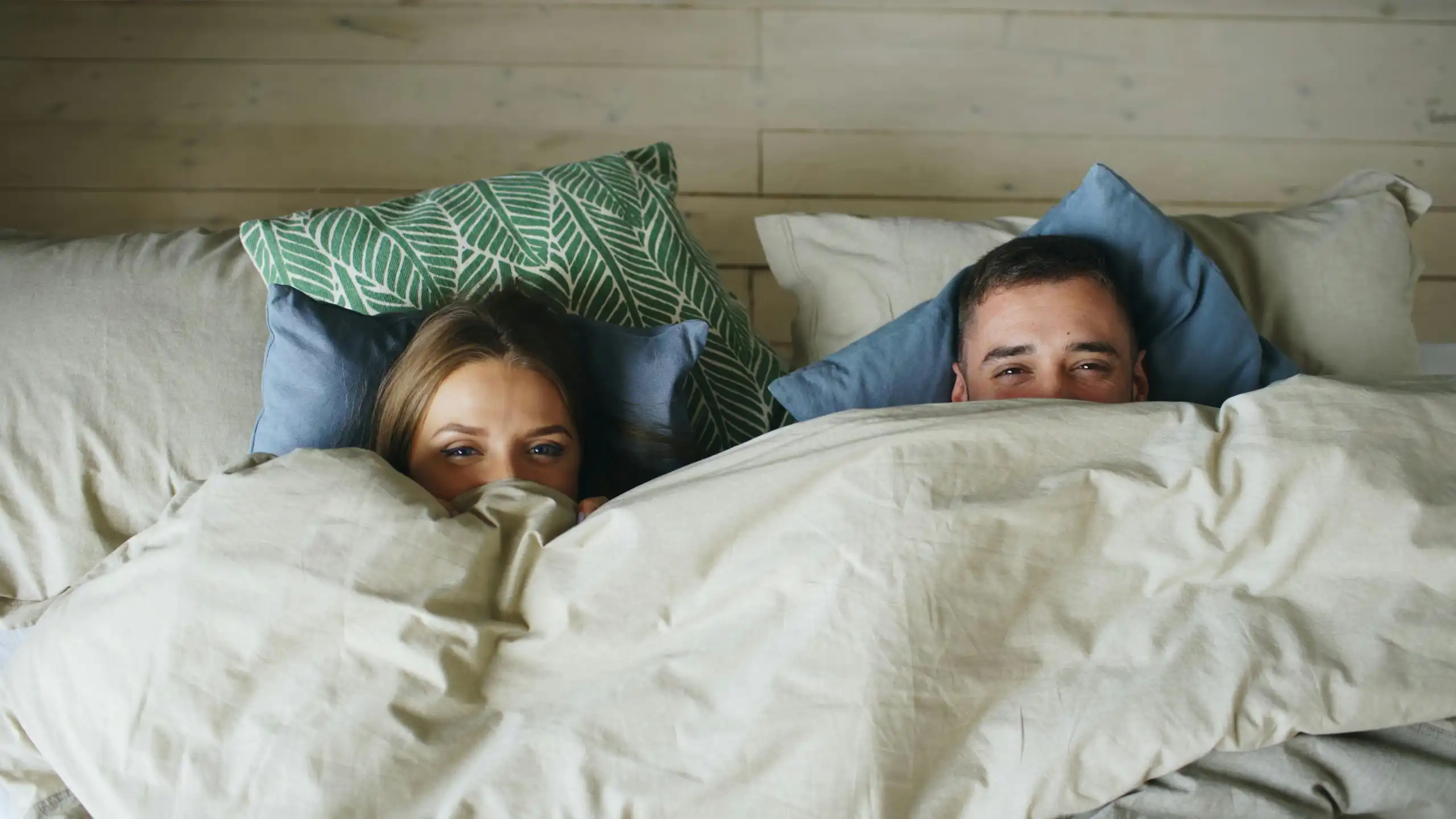 A couple lie in bed covered by a cosy duvet.