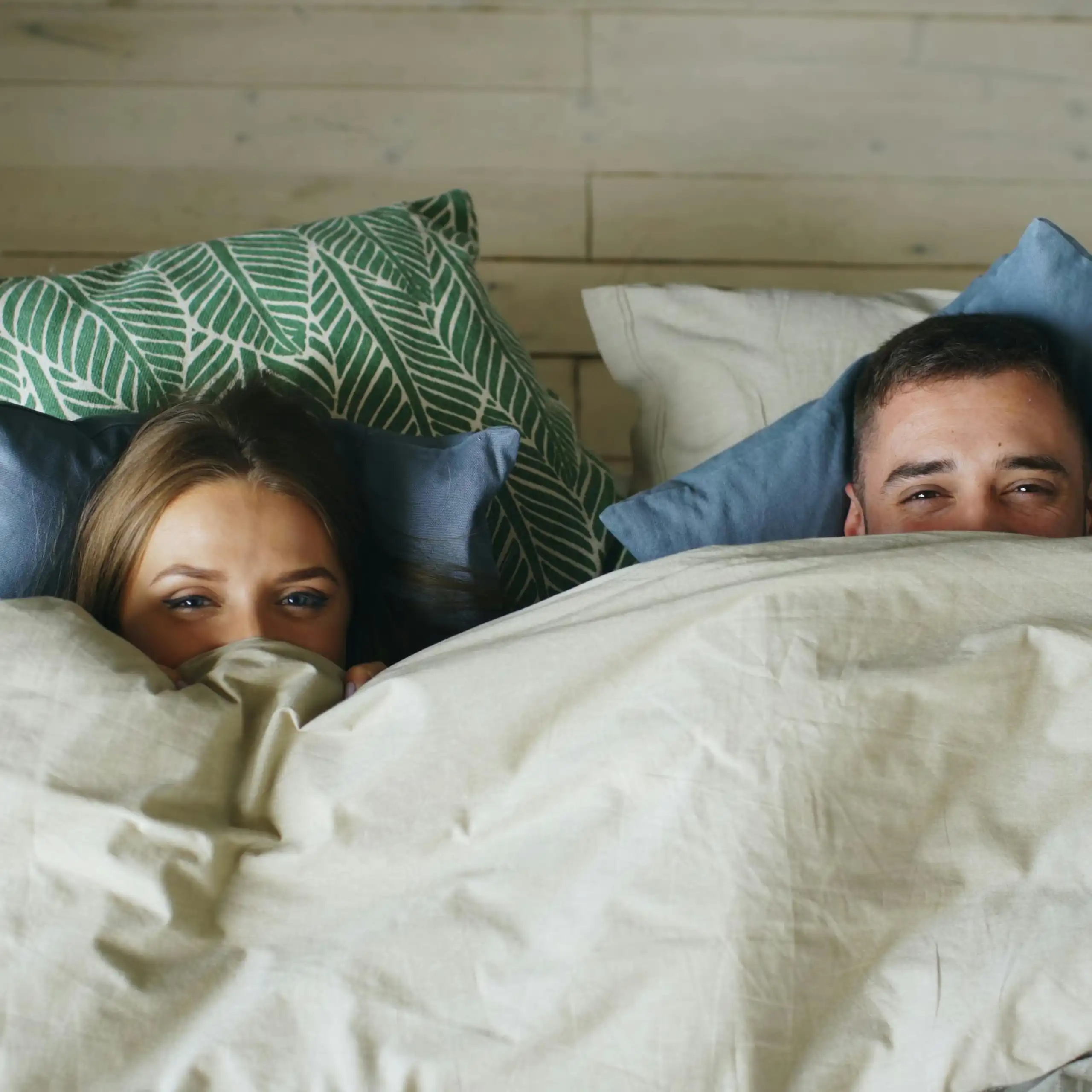 A couple lie in bed covered by a cosy duvet.