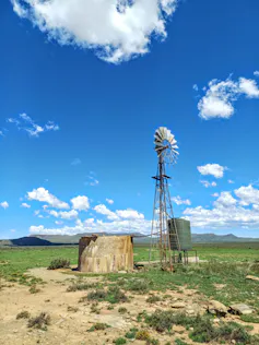 One windmill next to a concrete container set against a bright blue sky