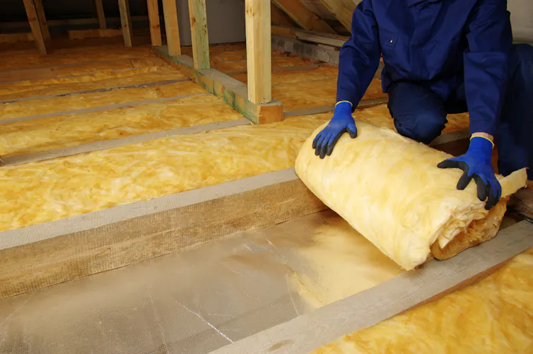 A person wearing gloves unrolls some insulation.