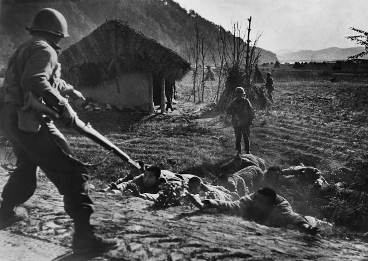 A soldier with a gun ordering soldiers on the ground to do something.