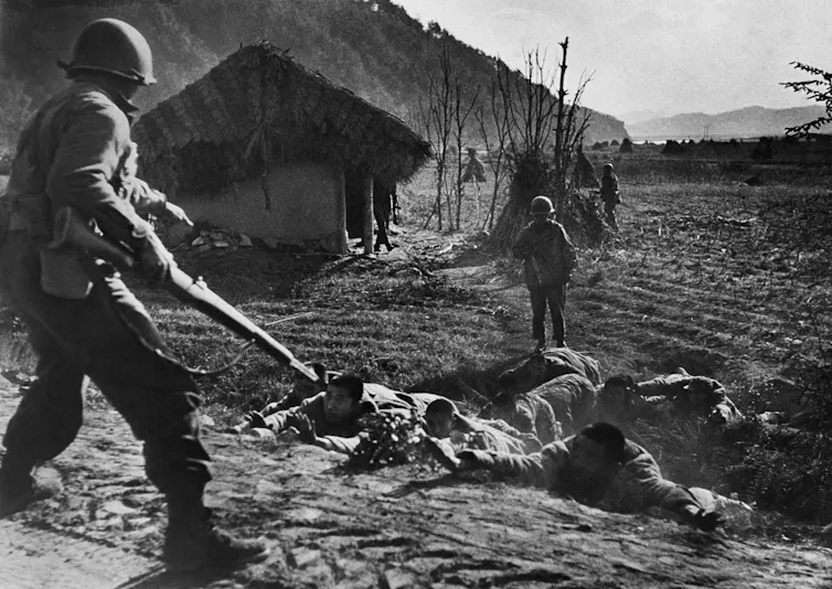 A soldier with a gun ordering soldiers on the ground to do something.