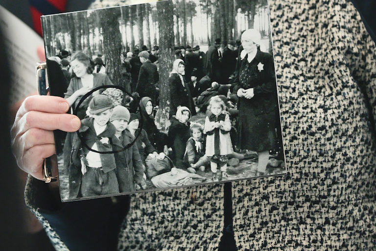 A person, seen from the neck down, holds up a black and white photo, with two boys wearing Jewish stars on their jackets circled in black marker.