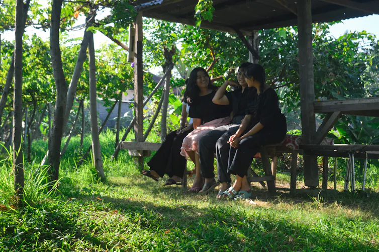 ¿Por qué el agua está mojada? 3 Un grupo de personas se sientan en un banco bajo una glorieta de madera en una zona de césped rodeada de árboles.