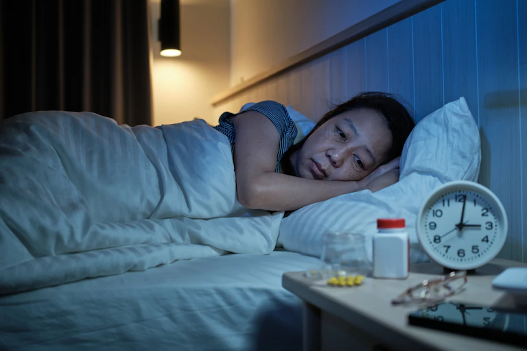 Uma mulher acordada na cama, ao lado de um relógio que marca 3 da manhã