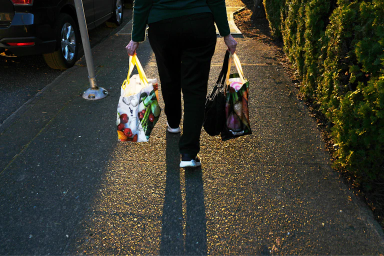 A person seen from the elbows down carries reuable shopping bags
