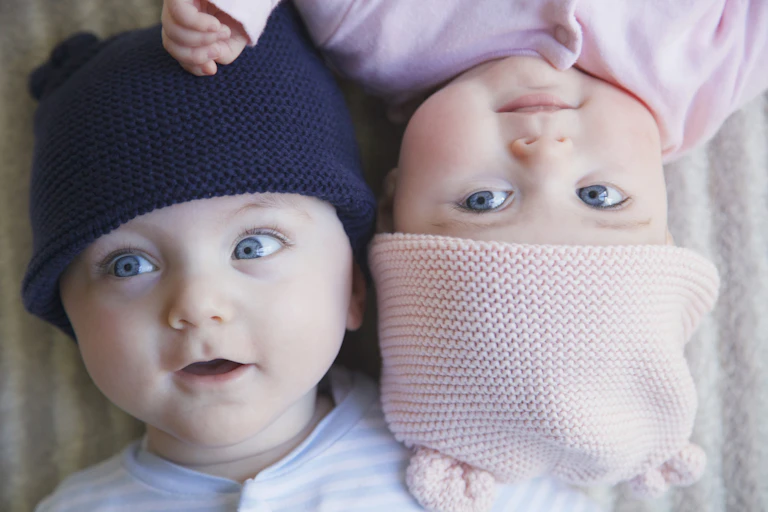 Elevated view of two babies, one in pink hat, one in navy blue, lying on backs facing opposite directions