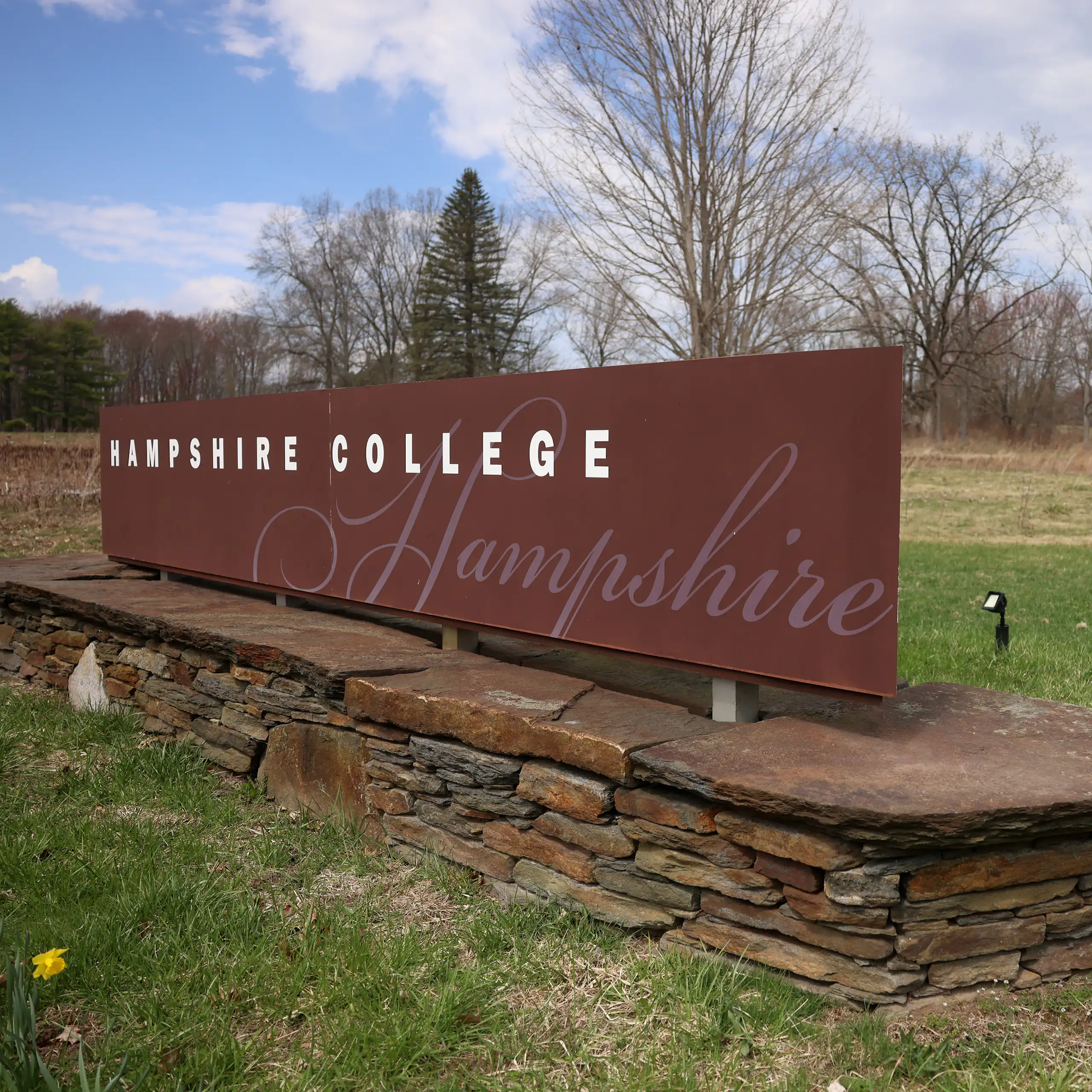 A brass sign mounted on a stone ledge on a grassy field says 'Hampshire College.'