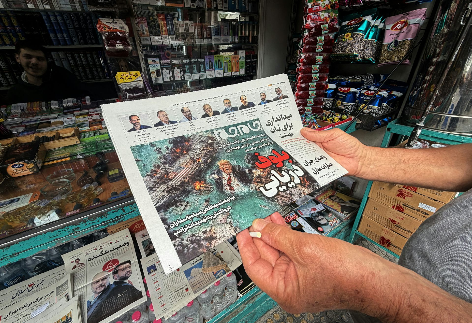 A man looks at the front page of the Jam Jam newspaper on sale at a newsstand, featuring a cartoon of US President Donald Trump drowning in the Strait of Hormuz with the headline 'Marine Bluff,' in Tehran