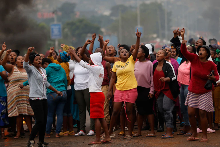 Group of people outdoors, some with arms raised, apparently singing or calling out