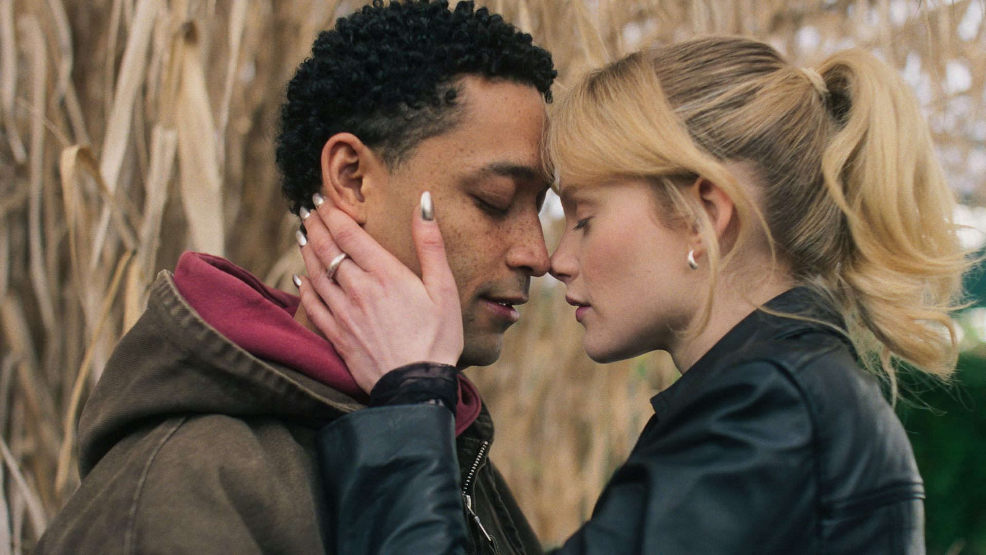 Loyle Carner and Emma Laird in a field of wheat. Emma holds Loyle's face in her hands.
