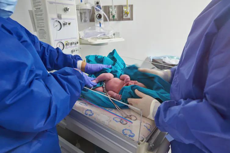 Two clinicians in scrubs holding newborn in a bassinet after cutting the umbilical cord