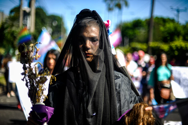Uma manifestante com um véu preto caminha por uma rua.