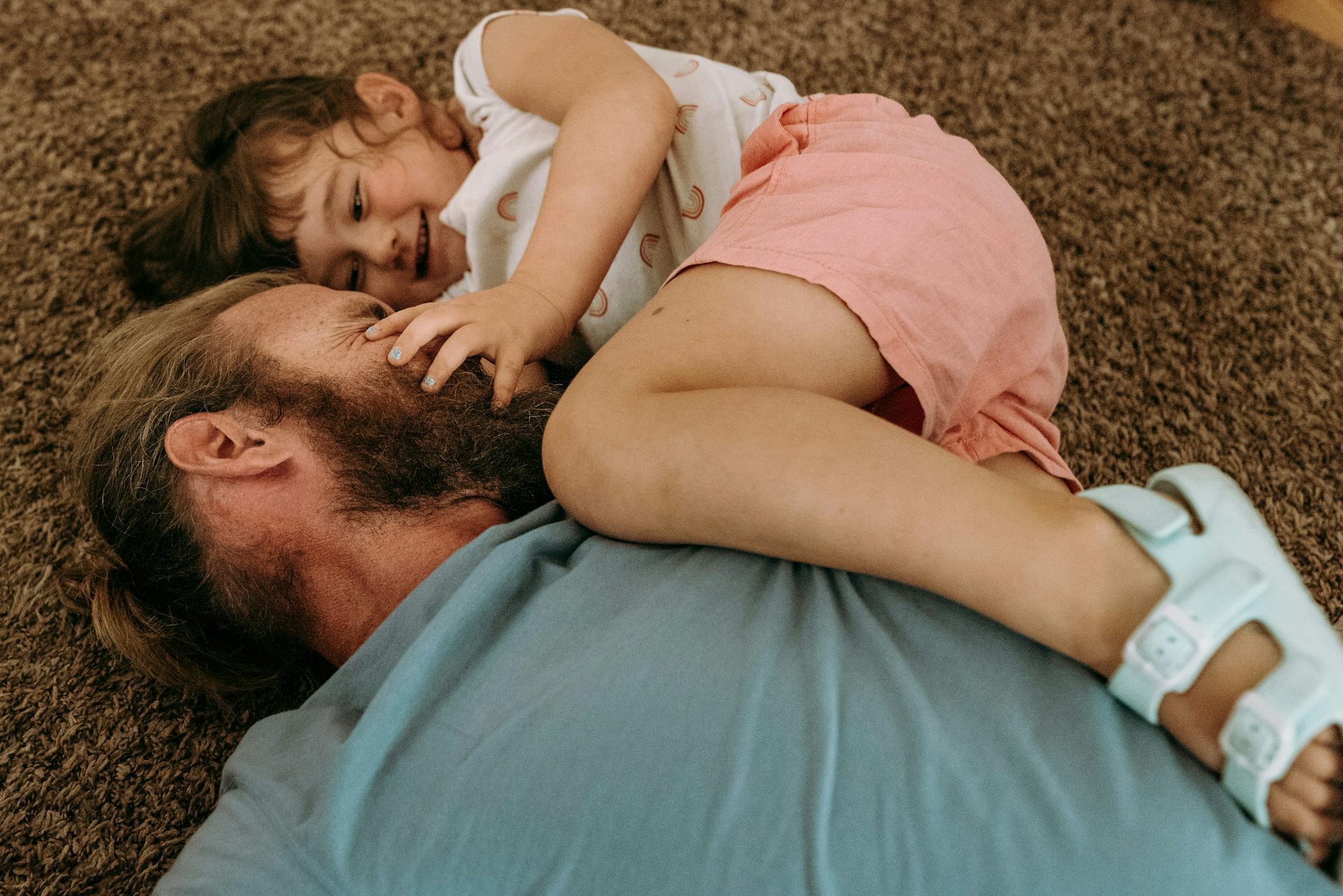 A parent playing around with their child on the carpeted floor as the child smiles.