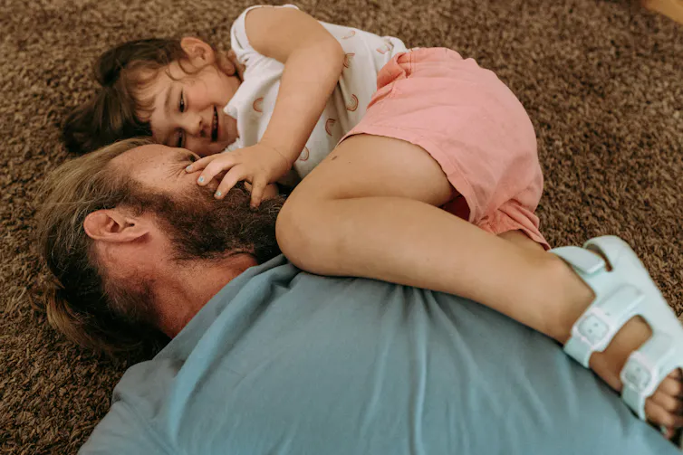 A parent playing around with their child on the carpeted floor as the child smiles.