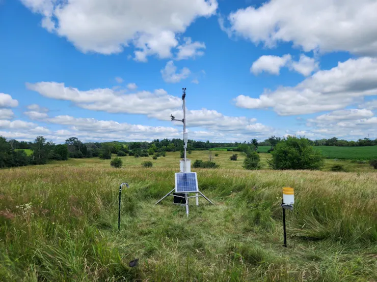 A tall tripod with various weather equipment and a solar panel for power.