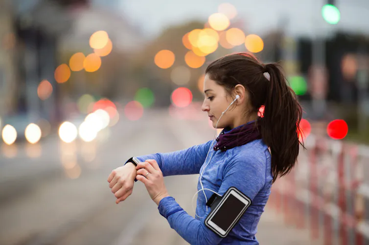a woman uses a smartwatch on her wrist, a smartphone is on her arm
