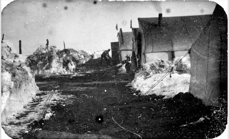 A black and white photograph of tents with piles of snow.