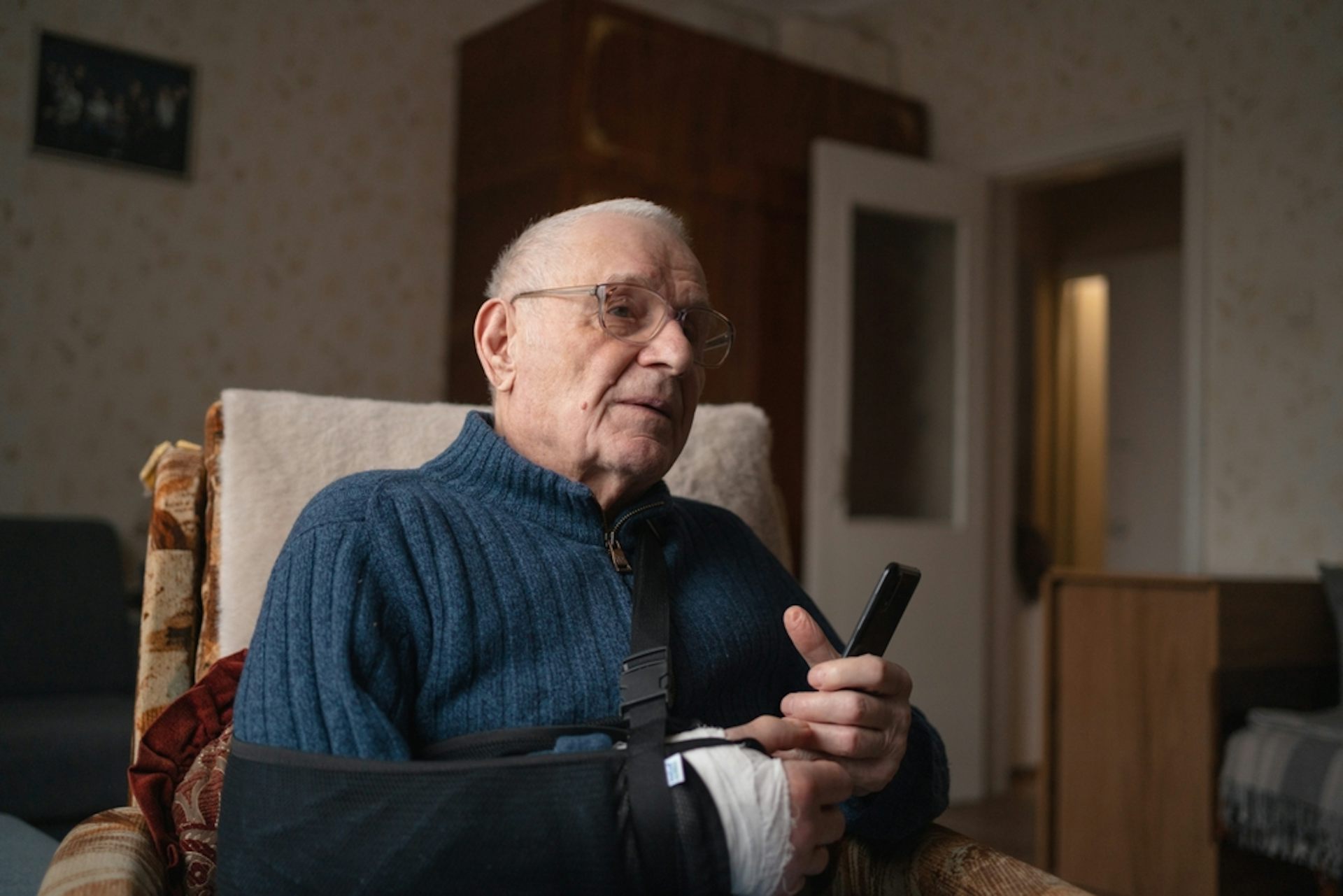 An elderly man with a broken arm, holding a mobile phone.