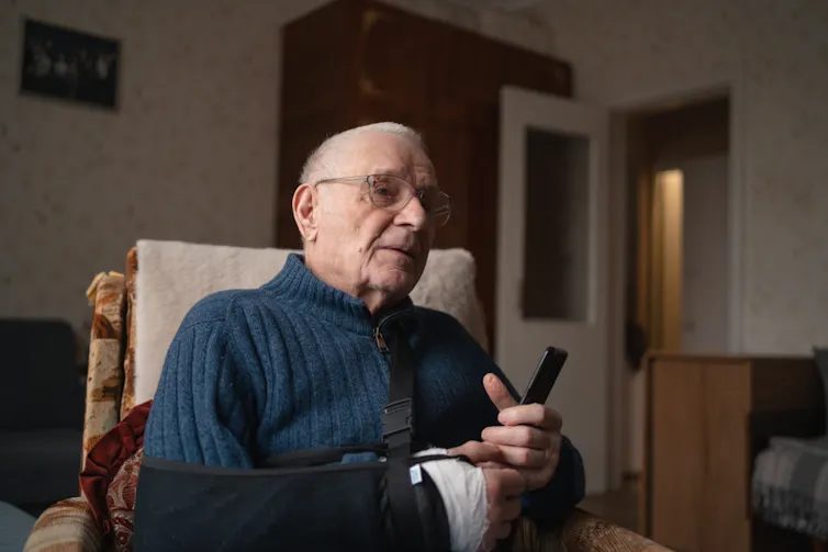 An elderly man with a broken arm, holding a mobile phone.
