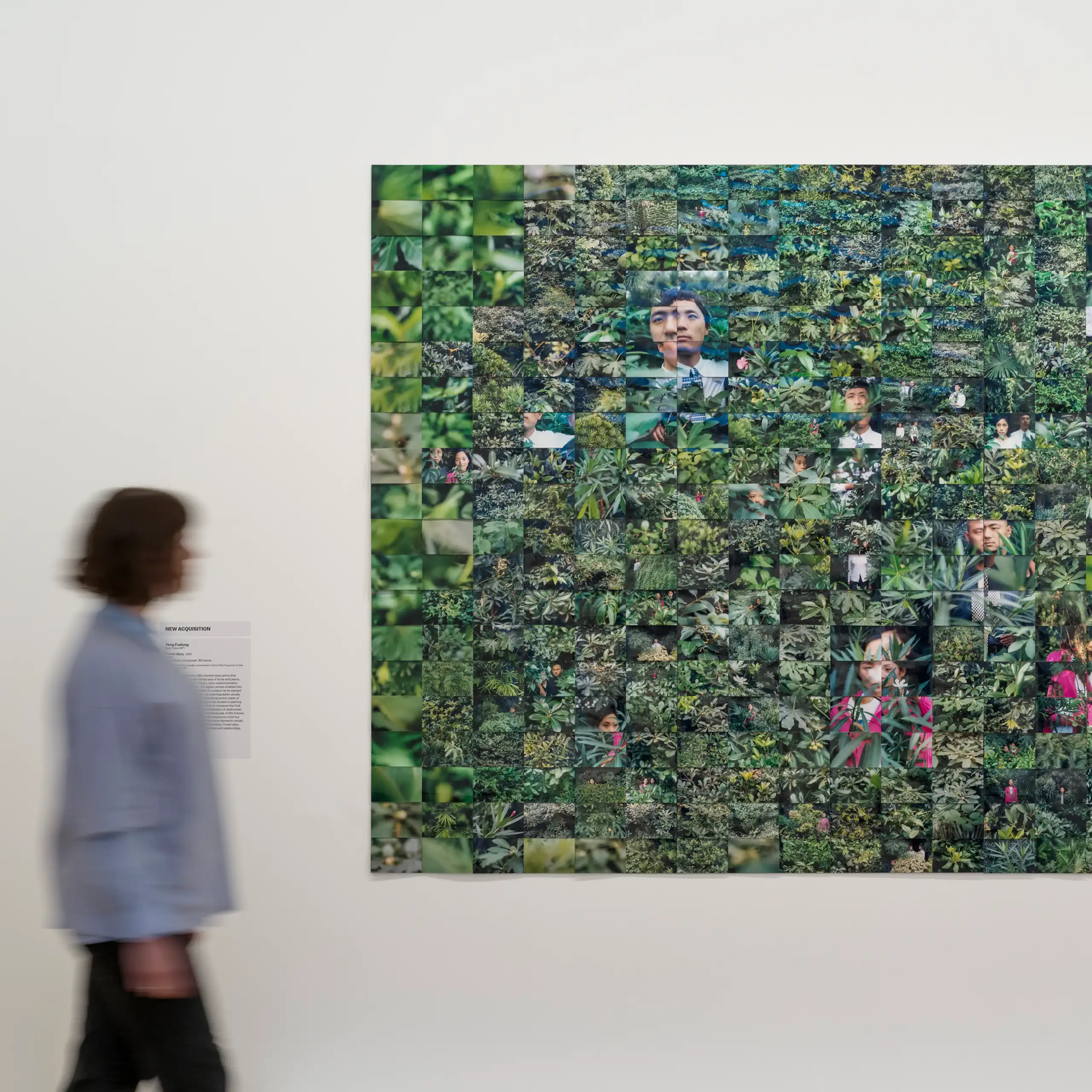 A woman walks past a collage of green photographs.