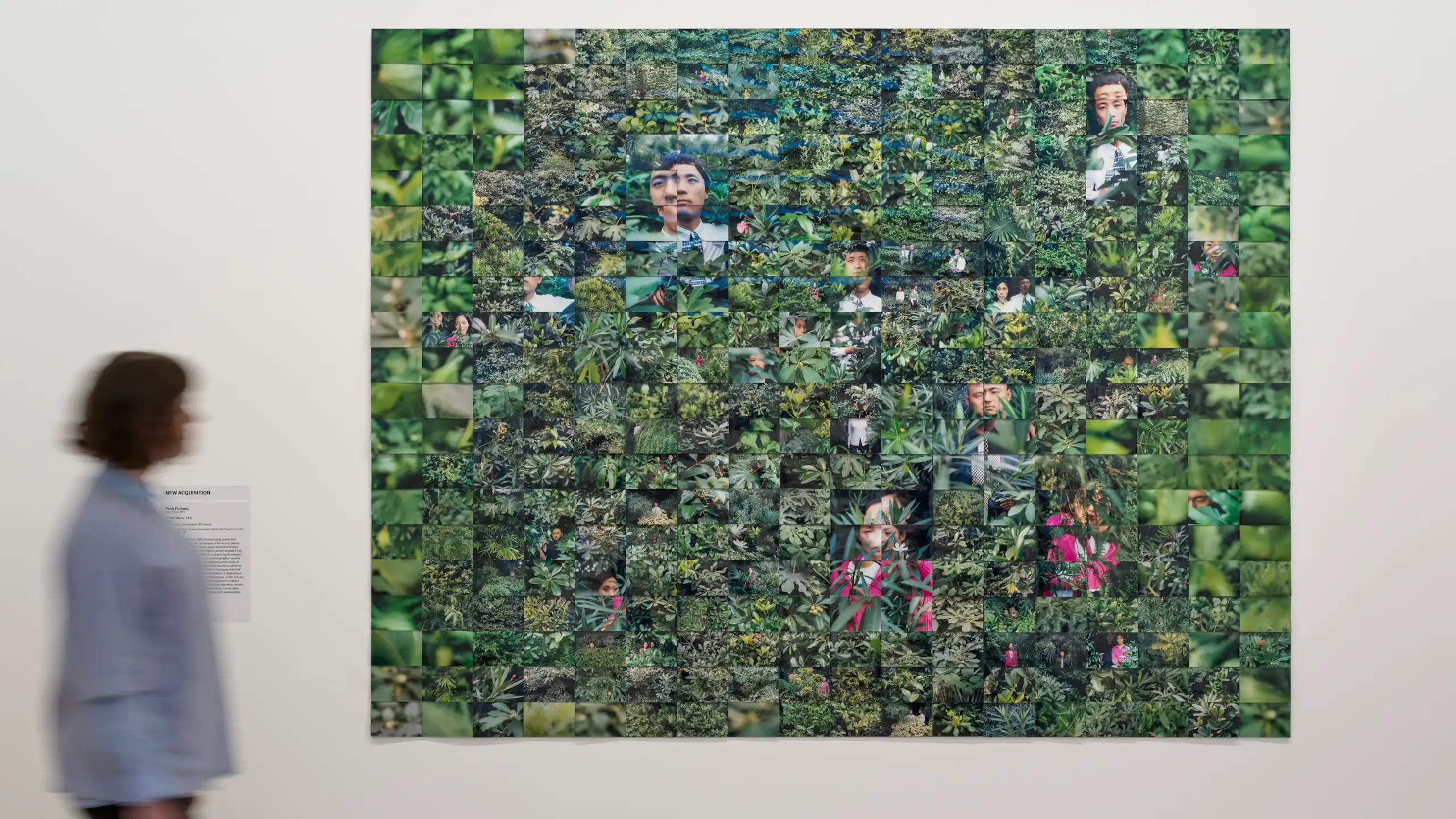 A woman walks past a collage of green photographs.