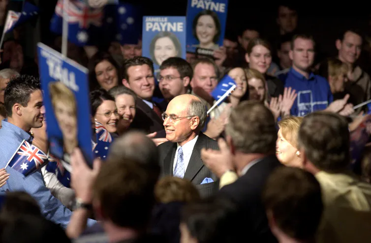 John Howard smiles broadly in the centre of a dense crowd of Liberal Party supporters