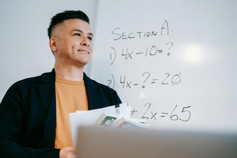A man holds papers in front of a whiteboard showing algorithms.