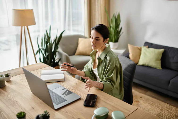 A woman in a green shirt speaks as in an online meeting at home