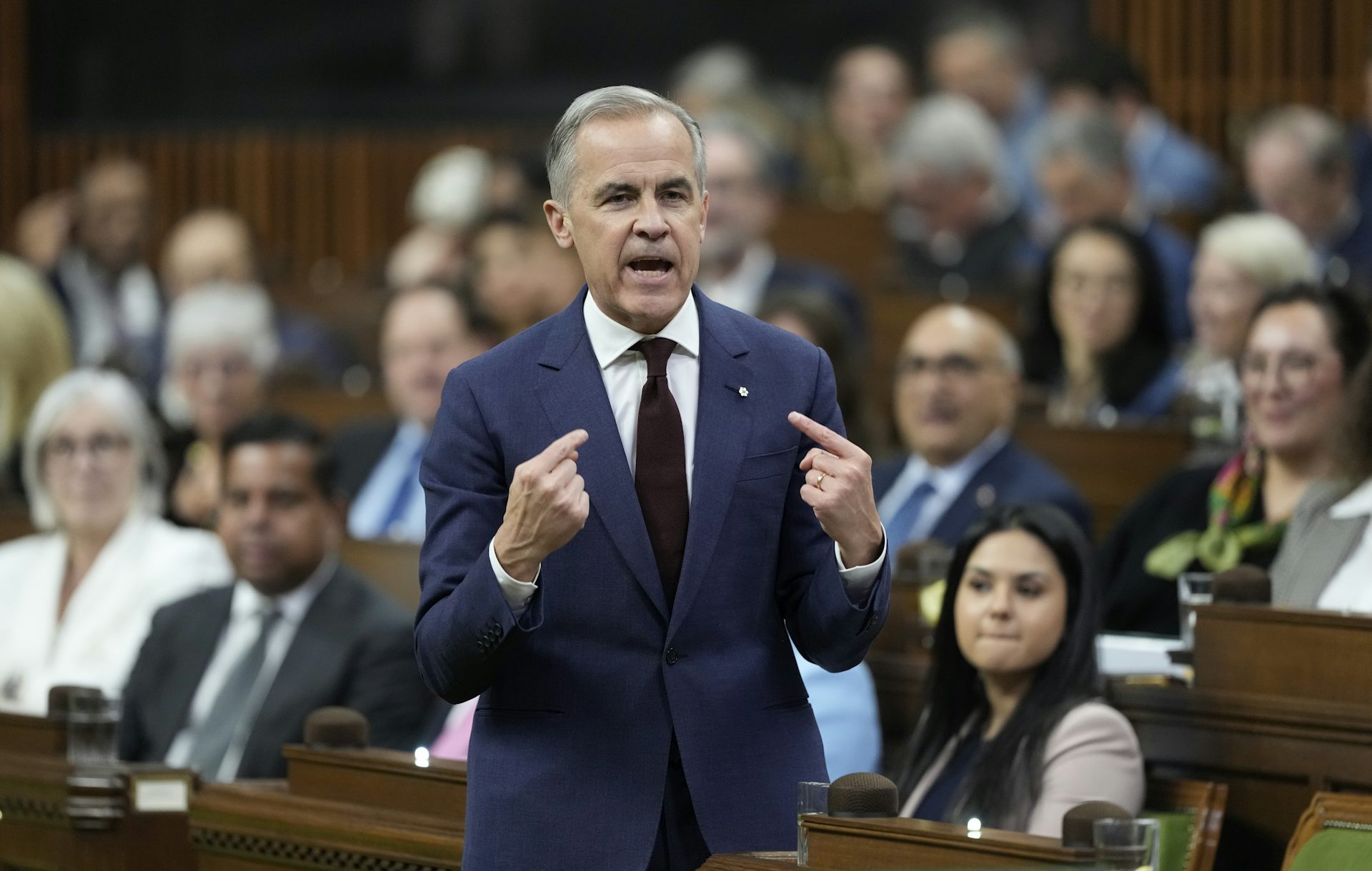 Un hombre delgado con cabello corto y oscuro se señala el pecho con el dedo índice mientras habla.