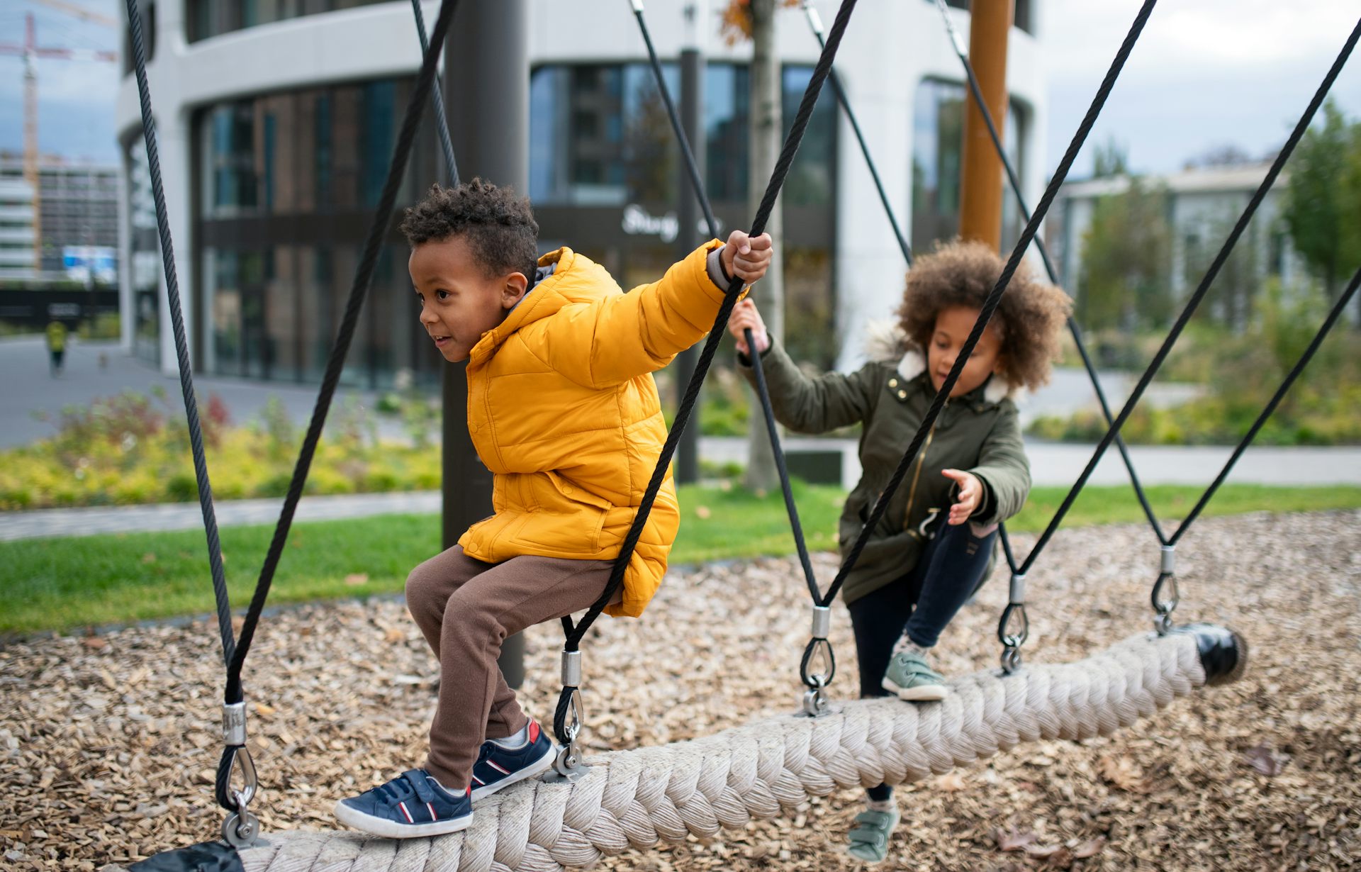 Two young children climb on ropes of playground equipment